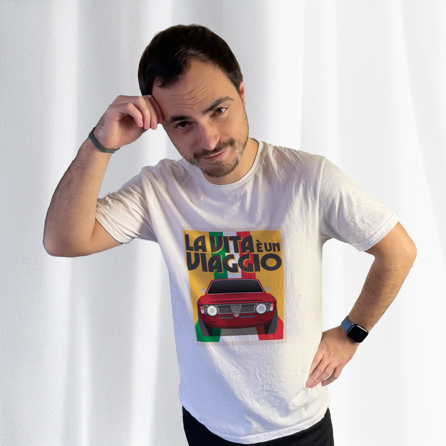T-shirt blanc avec au milieu une illustration type affiche "La Vita à un Viaggio" reprensentant une Alfa Romeo Giulia GT sur fond jaune de face roulant sur un drapeau italien qui par du fond pour se fondre sous la voiture, porté par Corentin Gouloumy