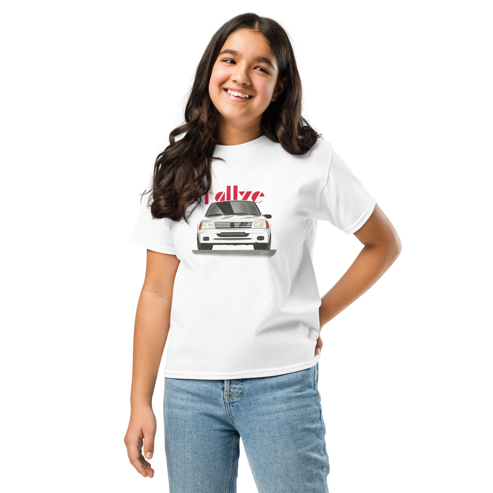 T-shirt blanc pour enfant avec le dessin d'une Peugeot 205 rallye blanche et le texte "rallye" rouge en fond porté par une fille