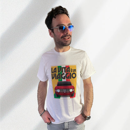 T-shirt blanc avec au milieu une illustration type affiche "La Vita à un Viaggio" reprensentant une Alfa Romeo Giulia GT sur fond jaune de face roulant sur un drapeau italien qui par du fond pour se fondre sous la voiture