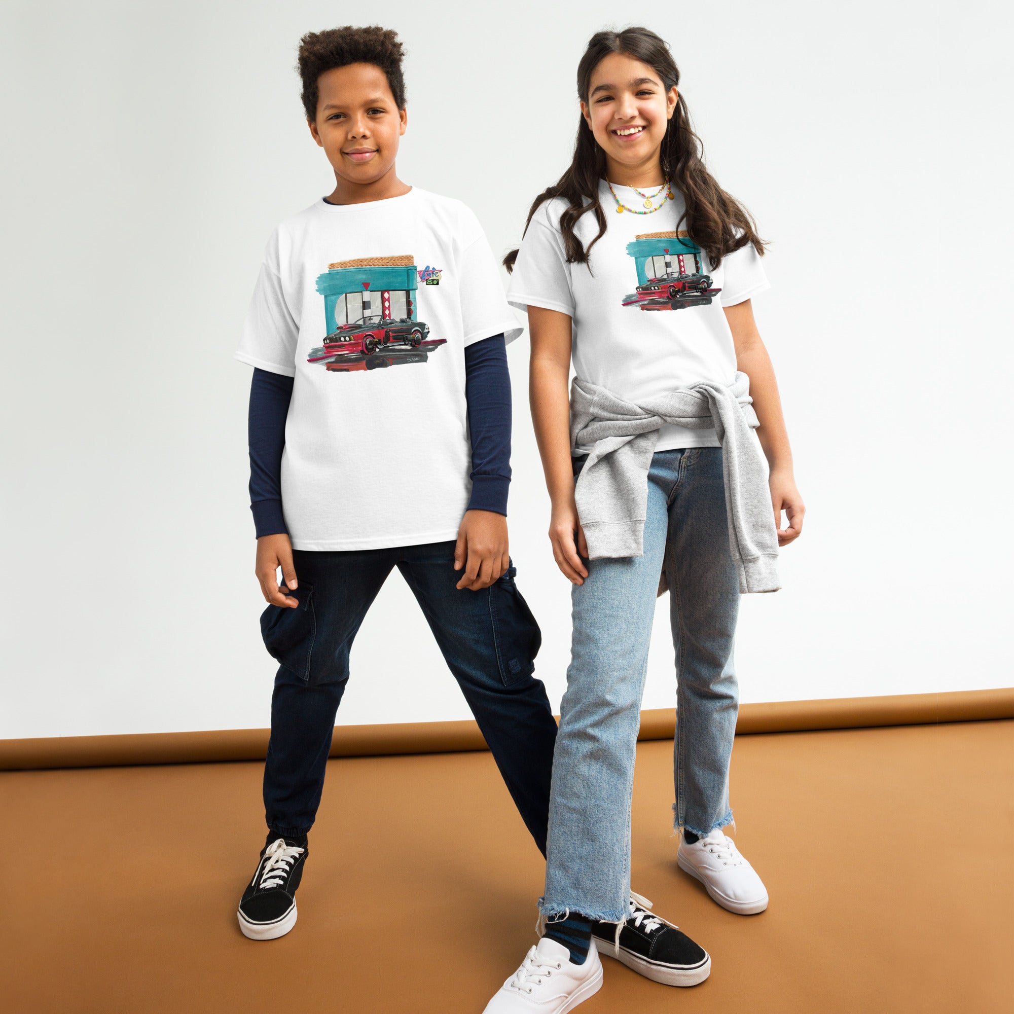 T-shirt enfant blanc avec une illustration de BMW devant un Café dans les 80s, reprenant le style de Retour vers le Futur, porté par des enfants