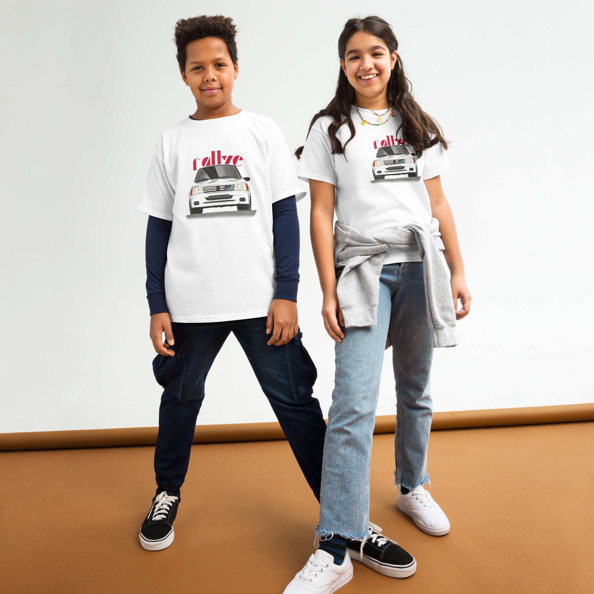 T-shirt blanc pour enfant avec le dessin d'une Peugeot 205 rallye blanche et le texte "rallye" rouge en fond porté par des enfants